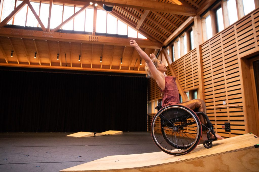 Alice Sheppard reaches her arms up into the arm to catch a moment of hangtime at the top of the wooden ramp before gravity pulls her backwards in her wheelchair. Photo by Hayim Heron; courtesy of Jacob's Pillow.