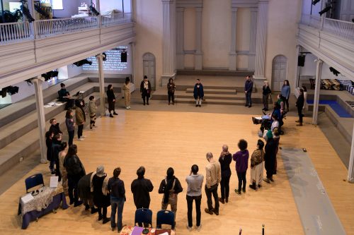A large circle of people standing on the floor of the church, facing in towards one another.