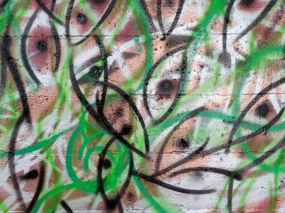 A spray painted abstract design. Many eye-like or fish-like shapes superimposed over each other. Colors are white, black, green, and brown.
