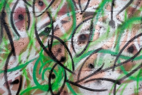 A spray painted abstract design. Many eye-like or fish-like shapes superimposed over each other. Colors are white, black, green, and brown.