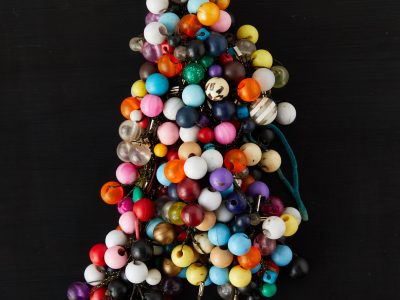 Sitting on a black background is an art object, a cluster of knotted hair-ties adorned with colorful plastic balls.