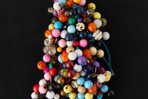 Sitting on a black background is an art object, a cluster of knotted hair-ties adorned with colorful plastic balls.